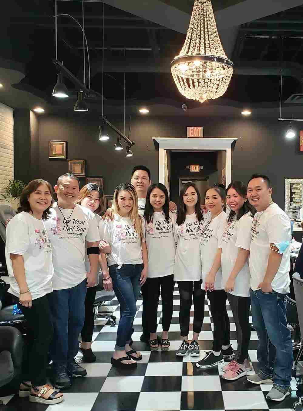 Group of salon team members in matching shirts posing together inside a nail bar.