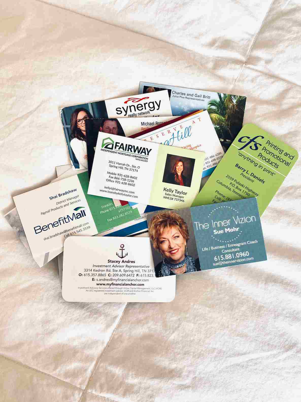Collection of business cards spread out on a white fabric surface.