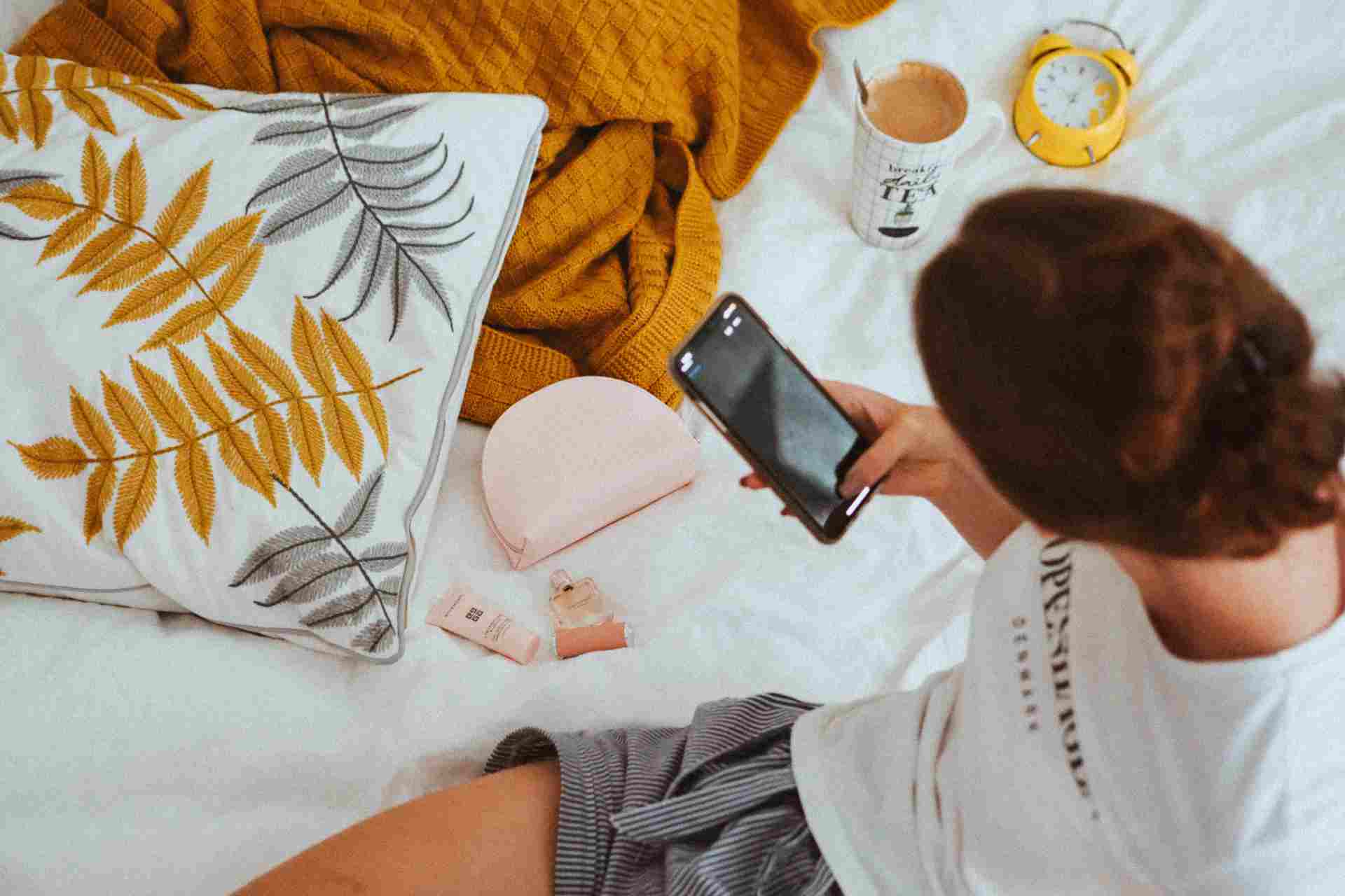 Person on bed with smartphone and personal items