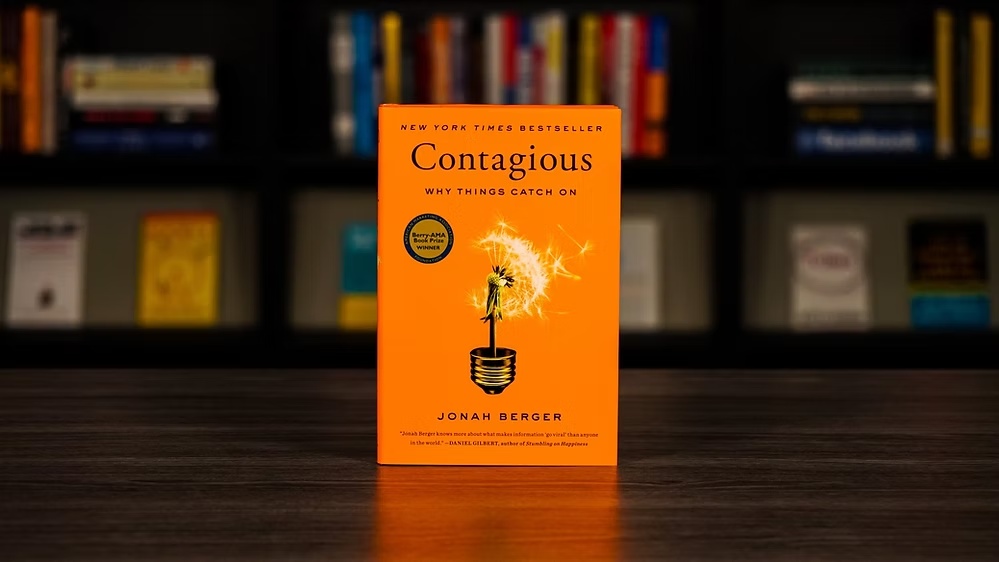 Book titled Contagious: Why Things Catch On by Jonah Berger with an orange cover featuring a dandelion illustration.