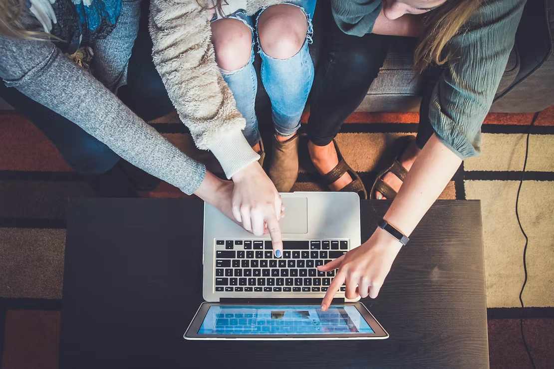 Group of three people collaborating and pointing at a laptop screen.