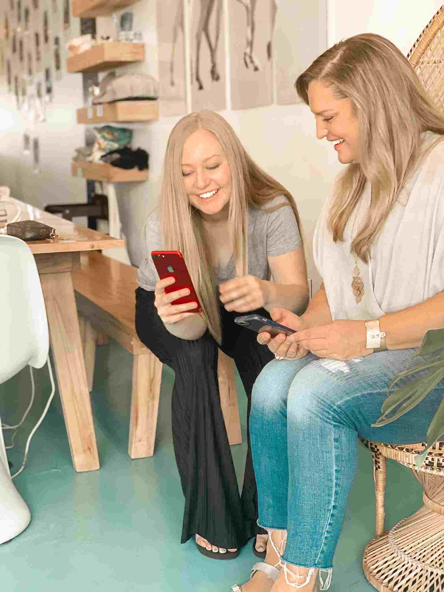 Two women smiling and looking at their phones during a relaxed meeting.