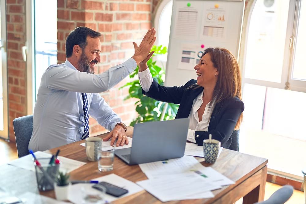 4 Steps to Content Planning for Social Media_post_image01 Two business professionals smiling and high-fiving at a meeting table.