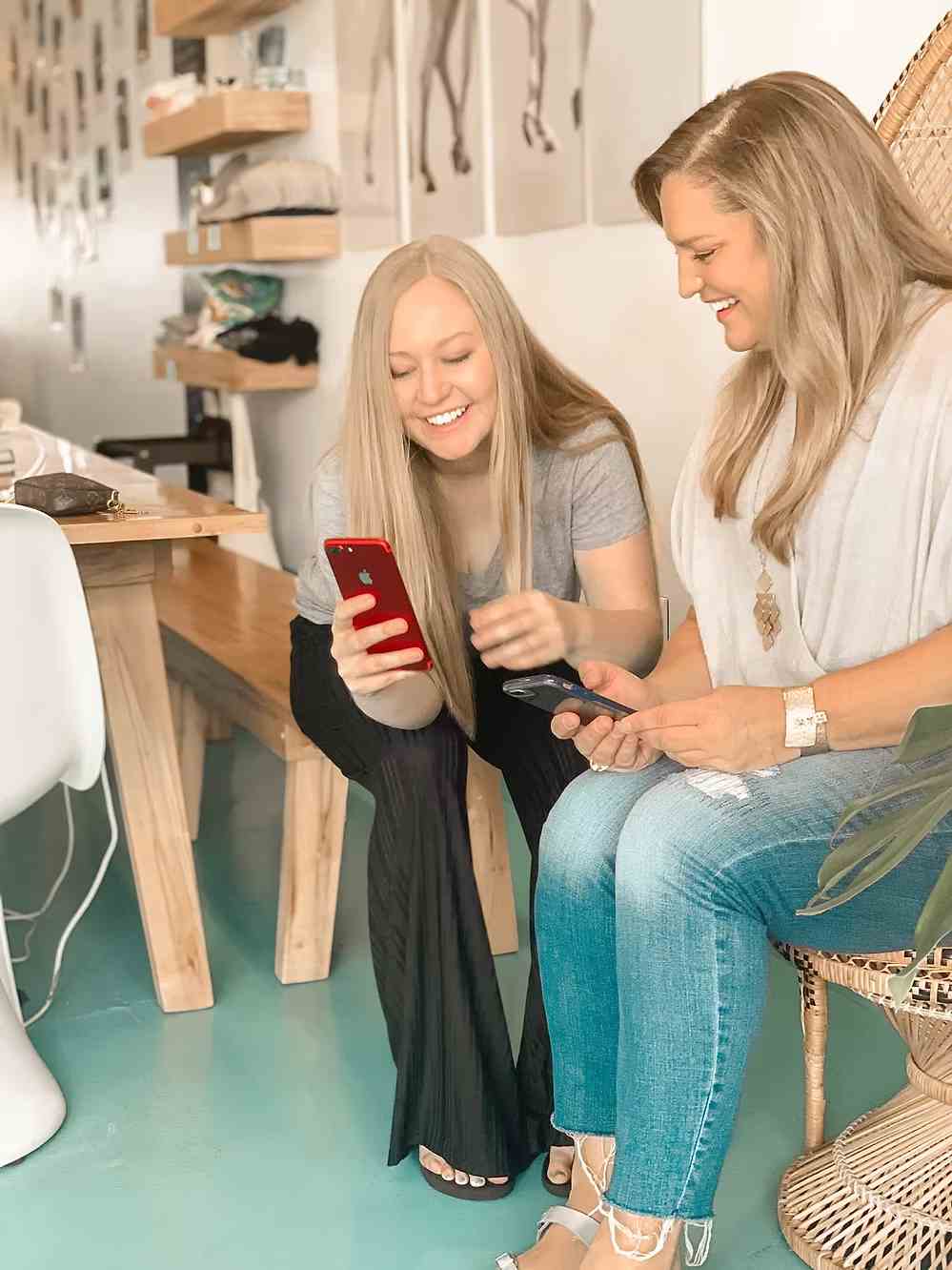 Two women smiling and looking at their phones during a relaxed meeting.