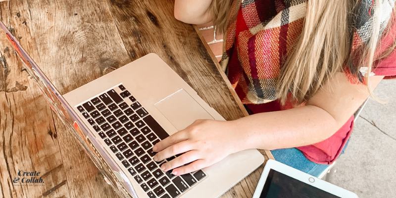 Woman working at a rustic wooden table on a laptop with a tablet beside her.