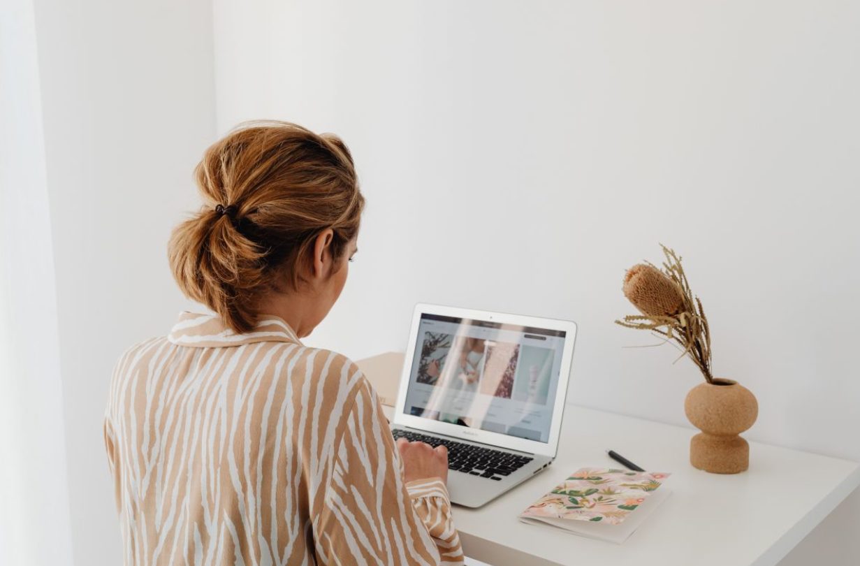 Woman with blonde hair in a zebra-patterned top working on a laptop at a minimalist white desk.