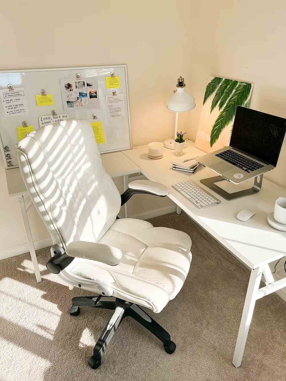 Bright home office setup with white desk, chair, laptop, and inspiration board.