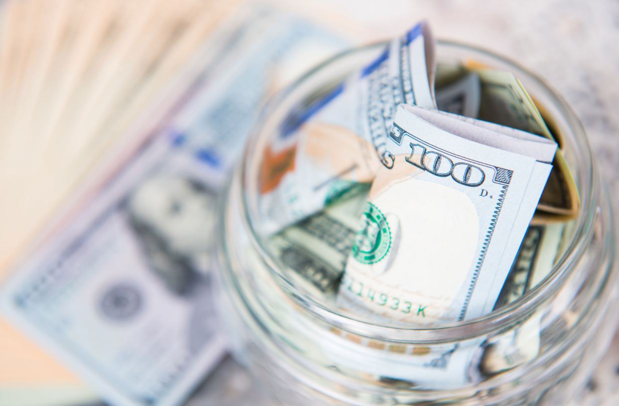 Close-up of a glass jar filled with folded hundred-dollar bills.