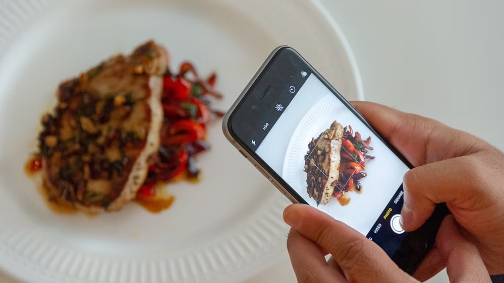 Person taking a close-up photo of plated food with a smartphone.