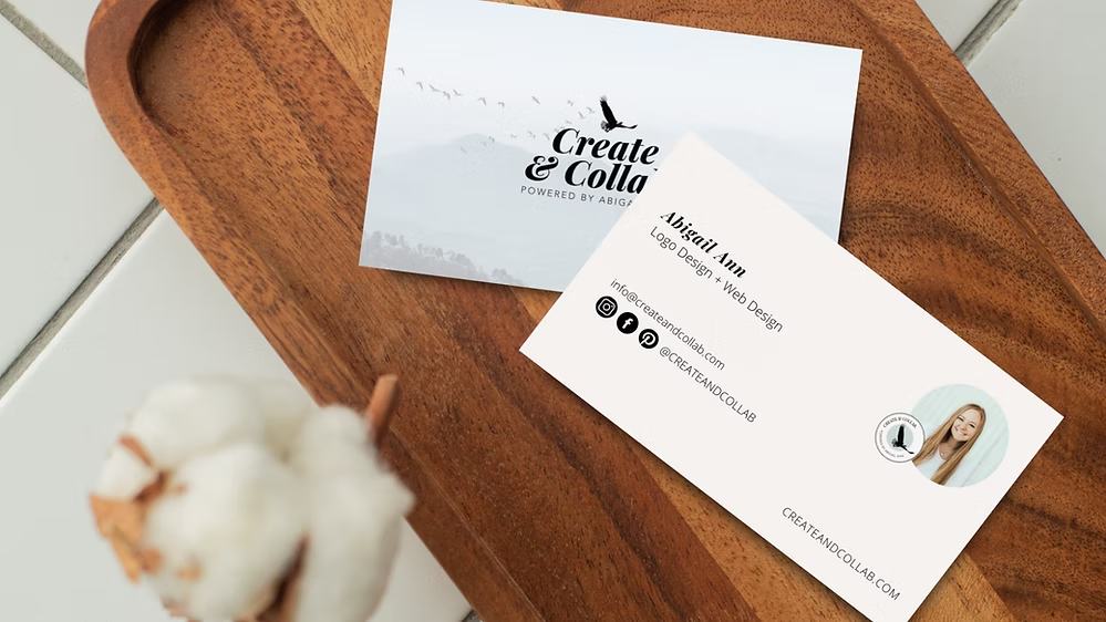 Create & Collab business cards displayed on wooden cutting board with cotton plant decoration.