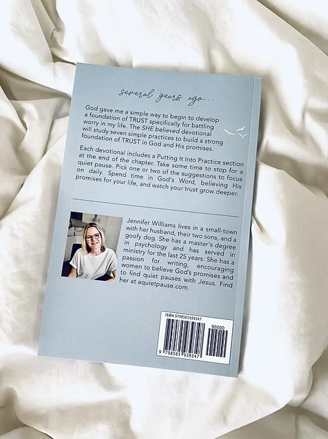Back cover of "She Believed" book showing author bio with photo and book description on white fabric.