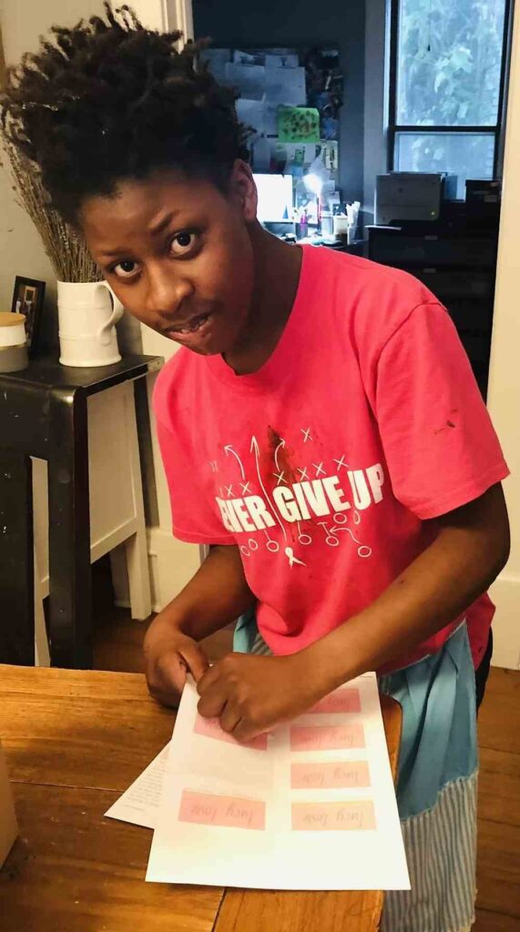 Person in red "Never Give Up" t-shirt working on colorful papers at wooden table in kitchen setting.