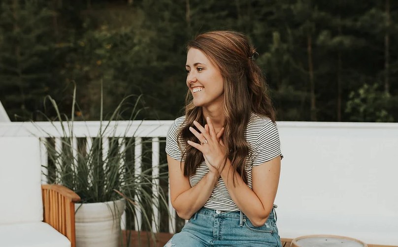 Woman smiling on an outdoor patio wearing a striped shirt and jeans.