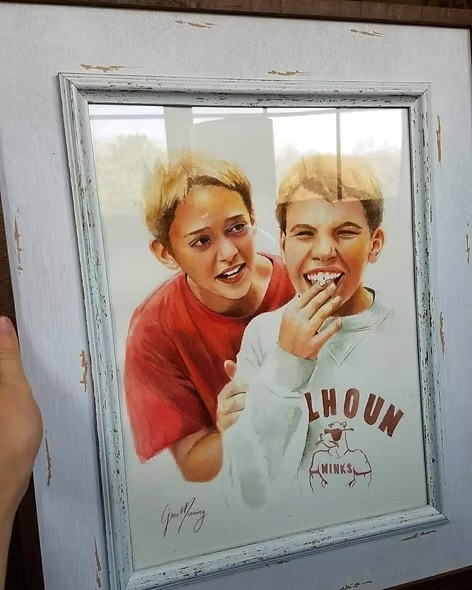 Framed watercolor portrait painting of two young boys embracing and smiling, displayed in distressed white frame.