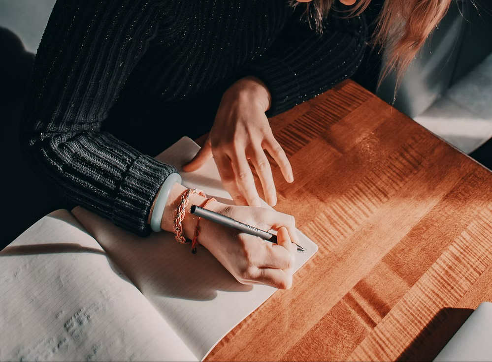 Person writing in notebook at wooden table
