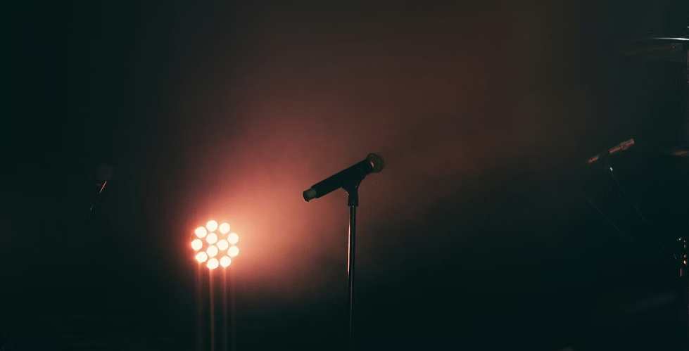 Microphone on a stand illuminated by warm stage lights in a dark, hazy atmosphere.
