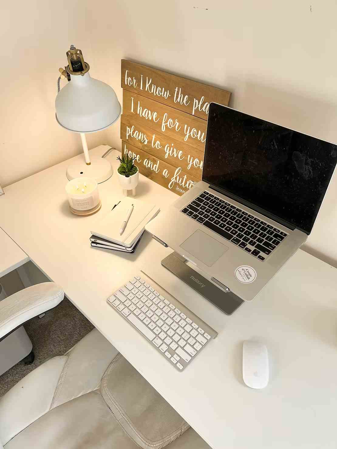 Laptop, keyboard, and notepads on a bright workspace with a motivational quote sign in the background.